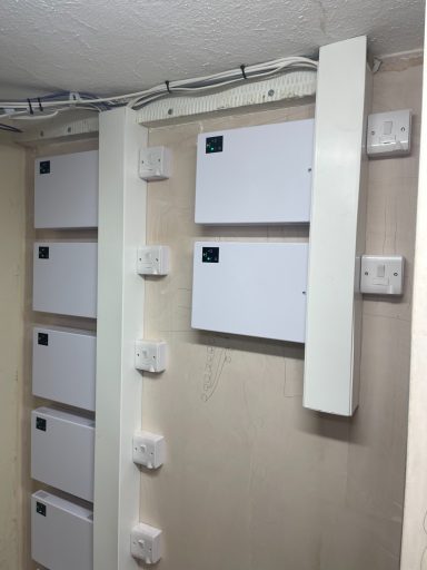 Row of white electrical boxes mounted on a wall, with cables and switches nearby.