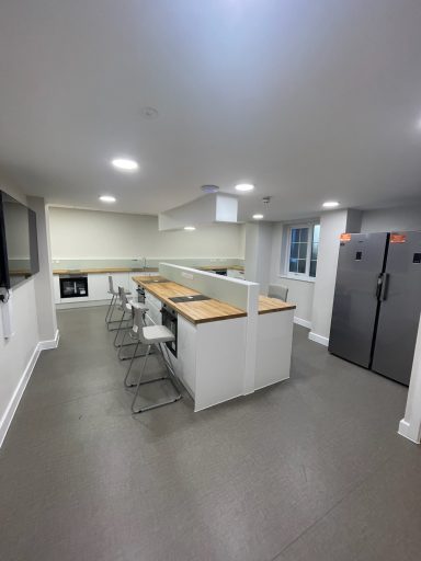 Modern kitchen with white cabinets, wooden countertop, bar stools, and grey flooring.