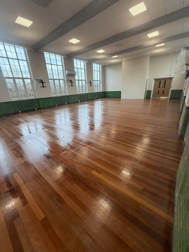 Empty indoor hall with polished wooden floor and large windows.