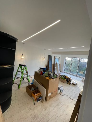Interior of a room in renovation, with tools, boxes, and a ladder under bright lights.