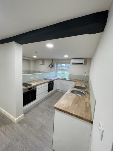 Modern kitchen with wooden countertops and white cabinetry, featuring a window for natural light.