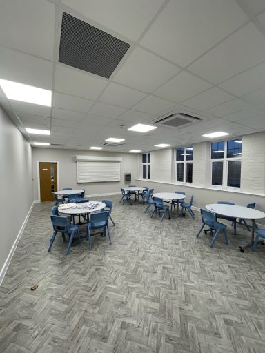 Bright classroom with light grey walls, round tables, and large windows.